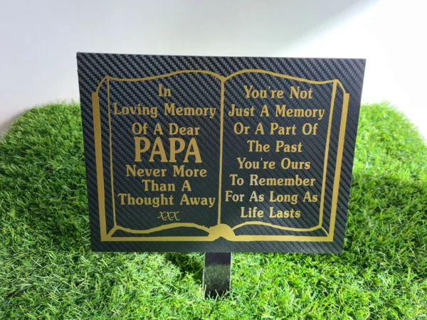 Black and gold papa plaque placed beside white grave flowers