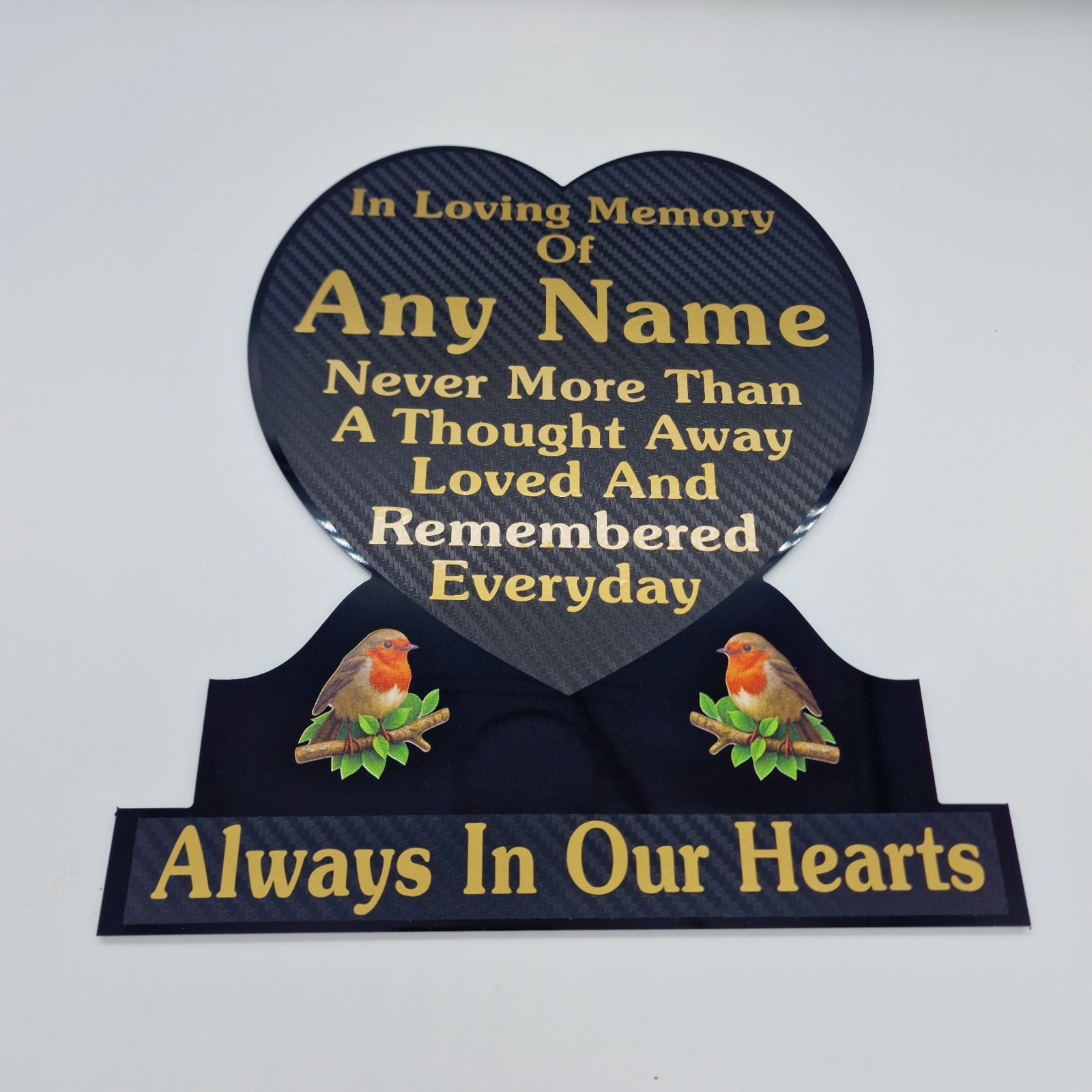 Close view of gold name and remembrance lettering and robin illustrations on a black heart-shaped memorial plaque.
